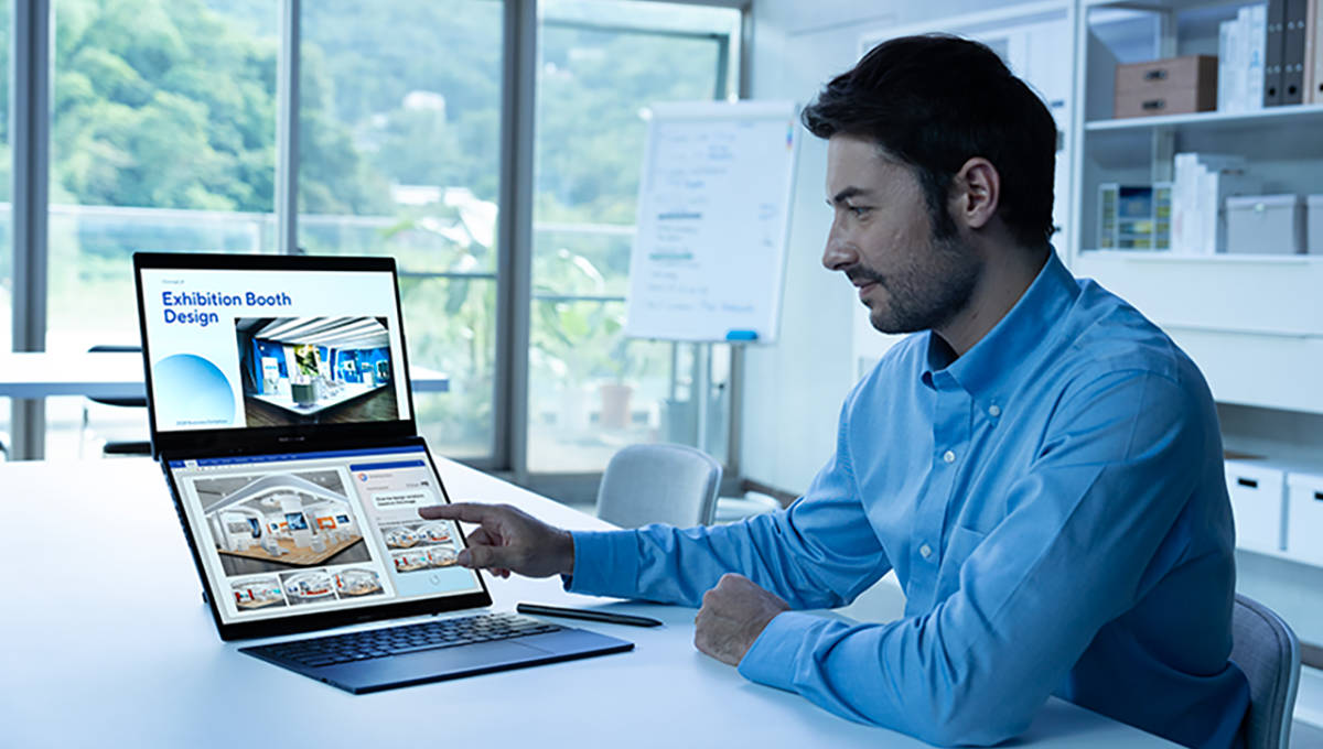 Mężczyzna w niebieskiej koszuli wskazujący na ekran laptopa Zenbook DUO w białej sali konferencyjnej. Na ekranie górnym wyświetlany jest jego główny projekt, natomiast ekran dolny jest podzielony na dwa okna.