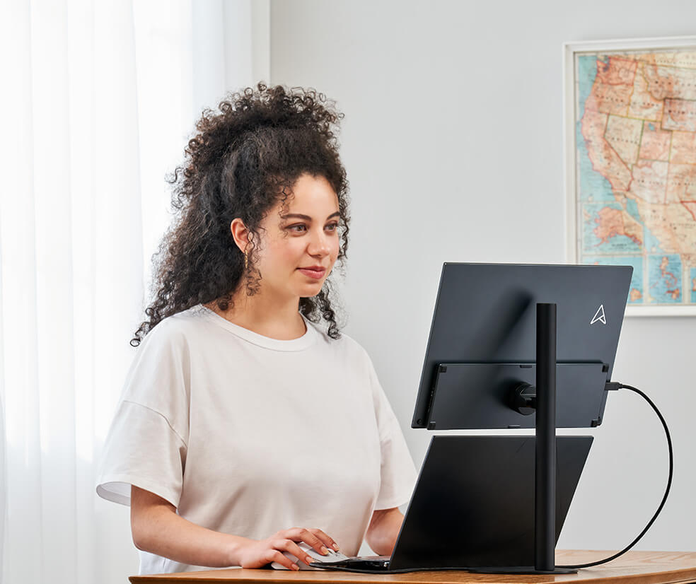 Kobieta pracuje w domu na z laptopie z podłączonym monitorem ZenScreen MB17AHG na statywie, dzięki czemu może patrzeć w ekran pod lepszym kątem.