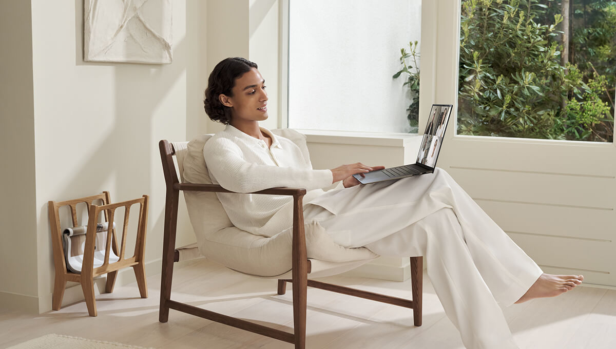 A man dressed in white is using Zenbook S 16 on his lap while sitting laid back on a classy looking chair.