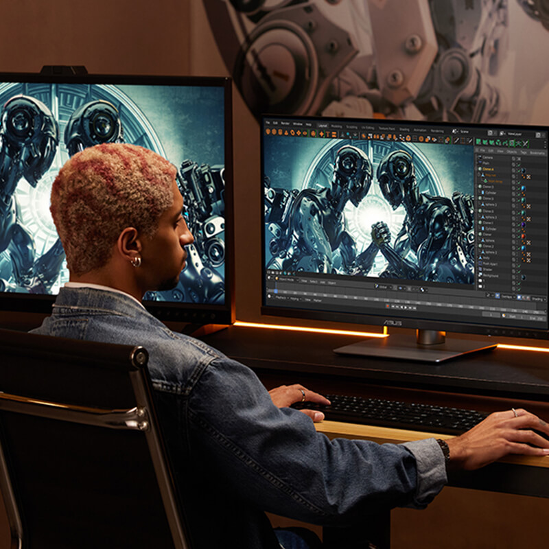 Een man zit op een stoel terwijl hij een ProArt-muis vasthoudt en typt op een toetsenbord met een externe ASUS ProArt-monitor aan de linkerkant en in het midden, en een ASUS ProArt station computer aan de rechterkant van het bureau.
