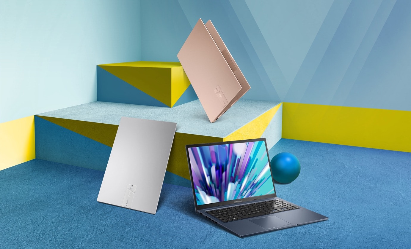 Three Vivobook 15 in Cool Silver, Terra Cotta, and Quiet Blue displaying around colored blocks with one opened in wide angle showing vivid display and two closed. 