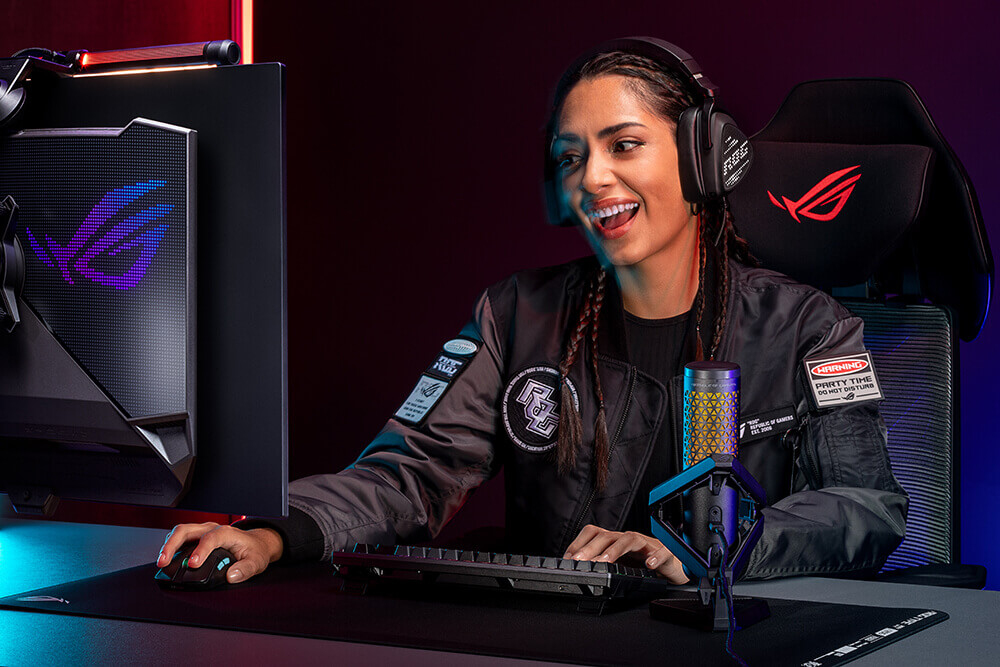 Smiling female gamer wearing a headset and gaming on a PC.