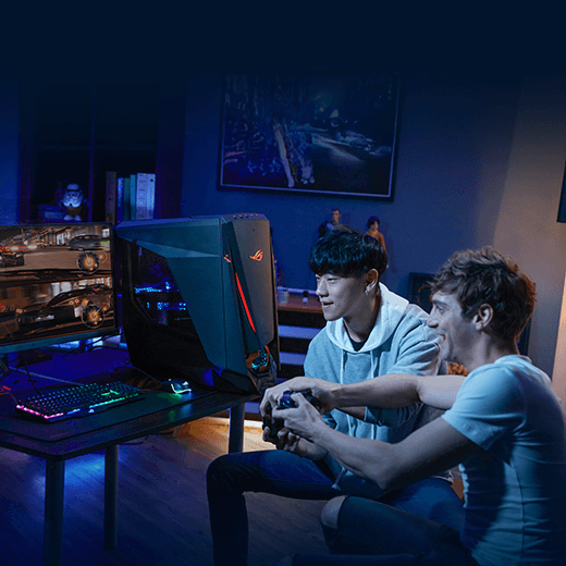 Two young men are enthusiastically playing a racing game on a dual-monitor setup connected to a ROG gaming PC