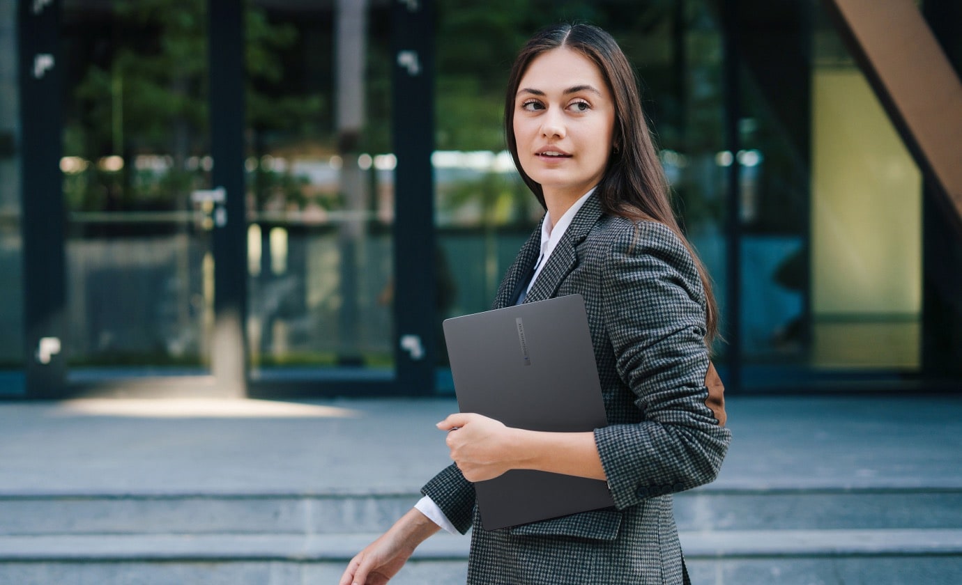 一位打扮偏商務感的女性, 手中拿著一台 ASUS ExpertBook B1 (B1403CVA)走在街道上​