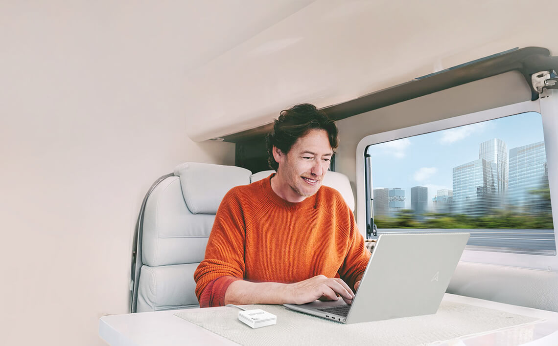 A man using laptop on a moving train, with a RT-AX50 Go on the table and the changing scenery visible through the window.