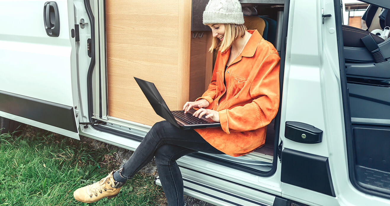 Une femme travaillant à distance sur un ordinateur portable, assise dans un camping-car, représentant un cadre de vie en camionnette.