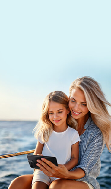 Une mère et son enfant assis sur le pont d'une croisière au bord de la mer, regardant un téléphone ensemble.