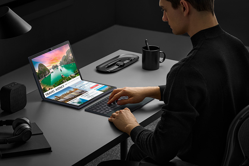 A man looks for information about travel agency on Zenbook 17 Fold OLED and types via the detachable ErgoSense Bluetooth keyboard. The OLED screen shows a beautiful scenery banner of the travel agency.