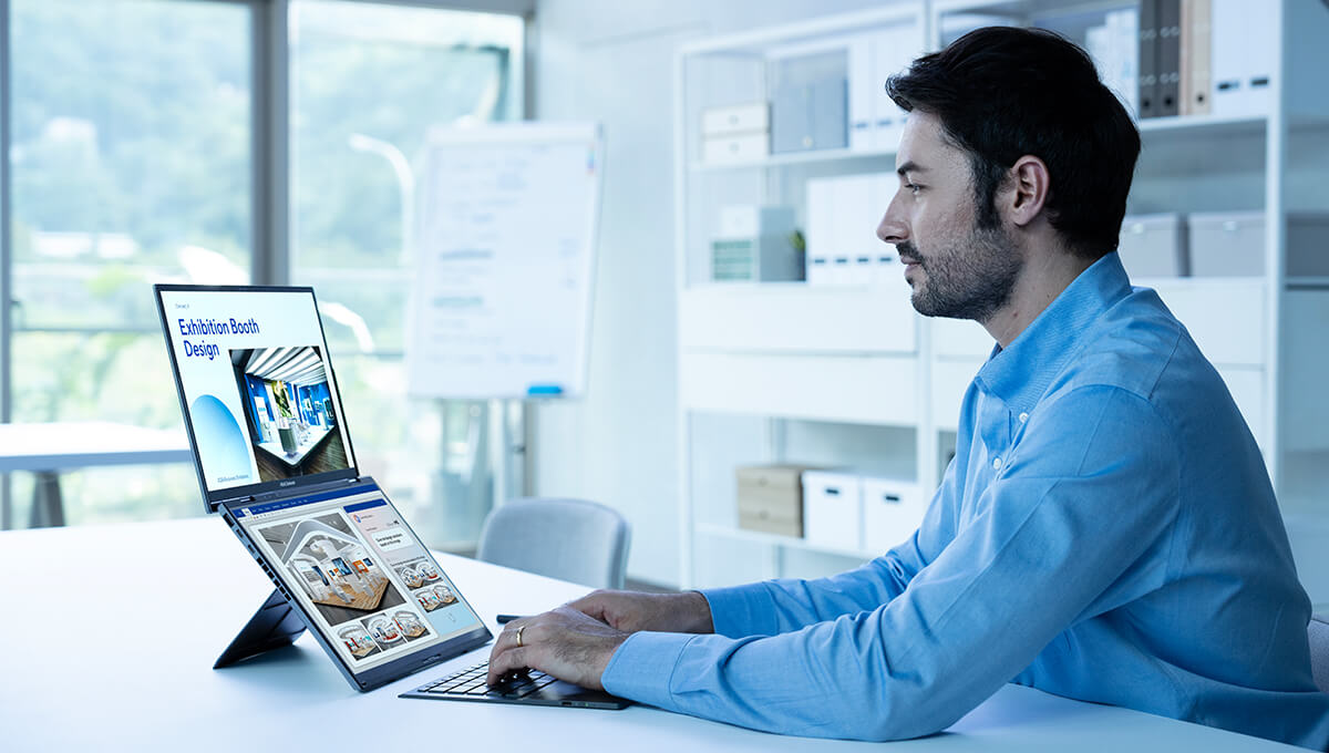 Un homme en chemise bleue tape sur le Zenbook DUO avec différentes informations affichées sur les écrans supérieur et inférieur.