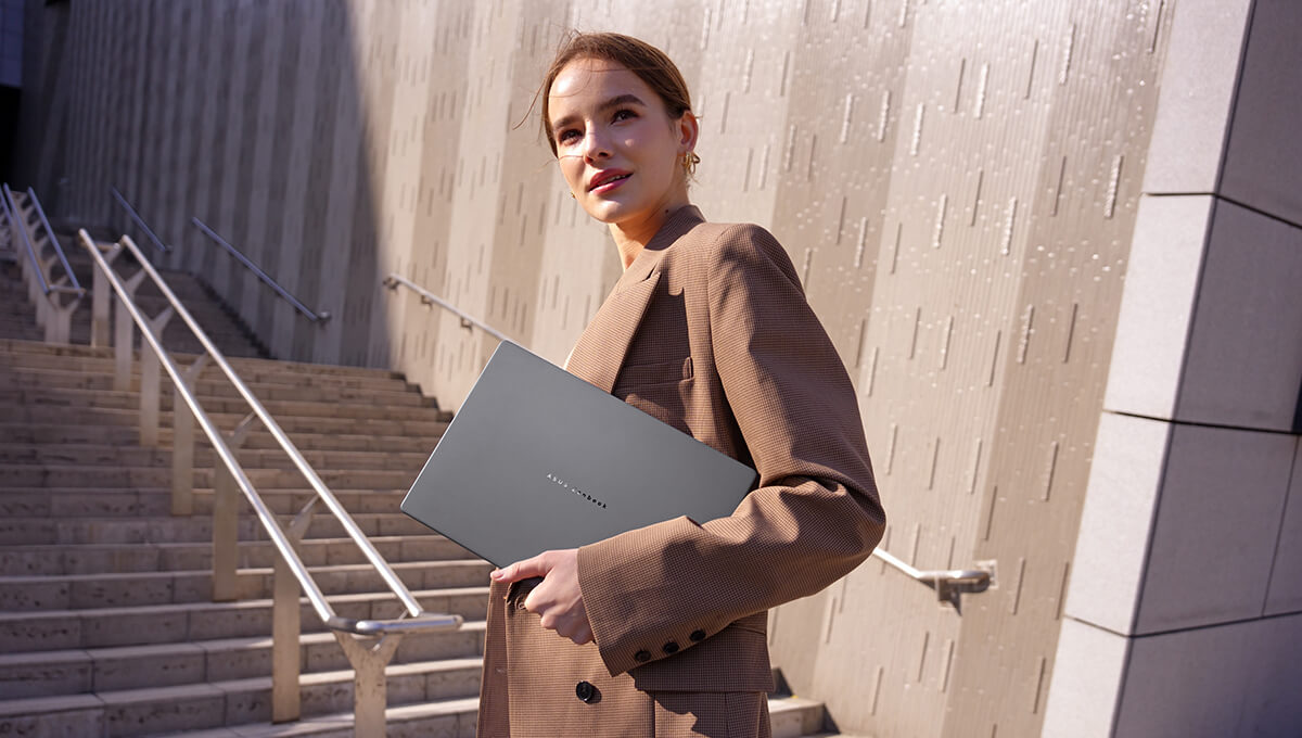 A woman in a brown coat has an Iceland Gray ASUS Zenbook A14 in her hand.