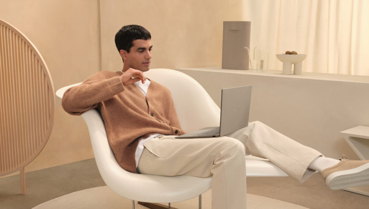 A young man sits on a modern looking white chair as he uses ASUS Zenbook A14.