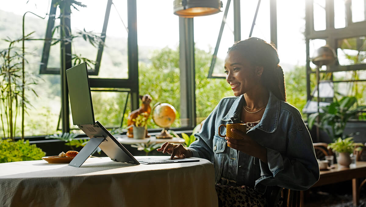 A woman using the ASUS Zenbook DUO laptop in a café while surrounded with plants