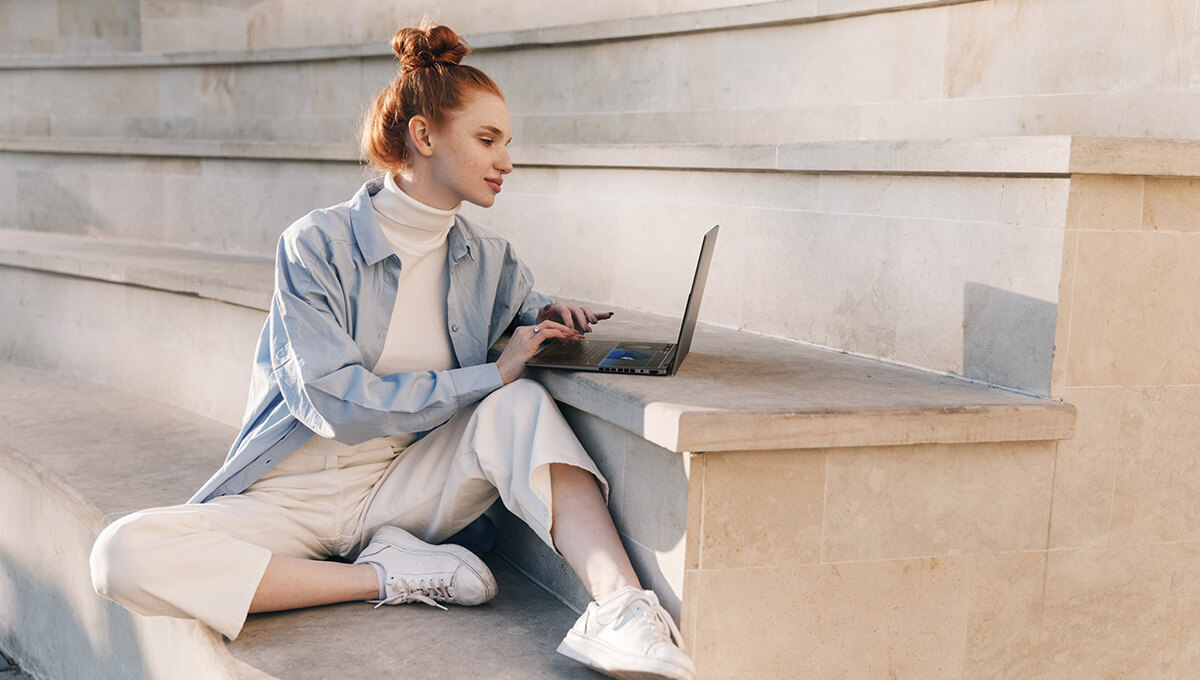 a woman using ASUS Zenbook DUO laptop while sitting on stairs outdoors