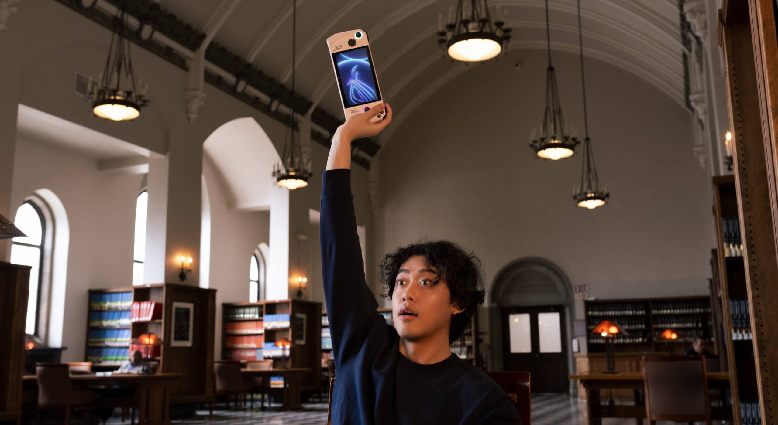 Person in a library holding an ROG Ally far above their head with one hand.