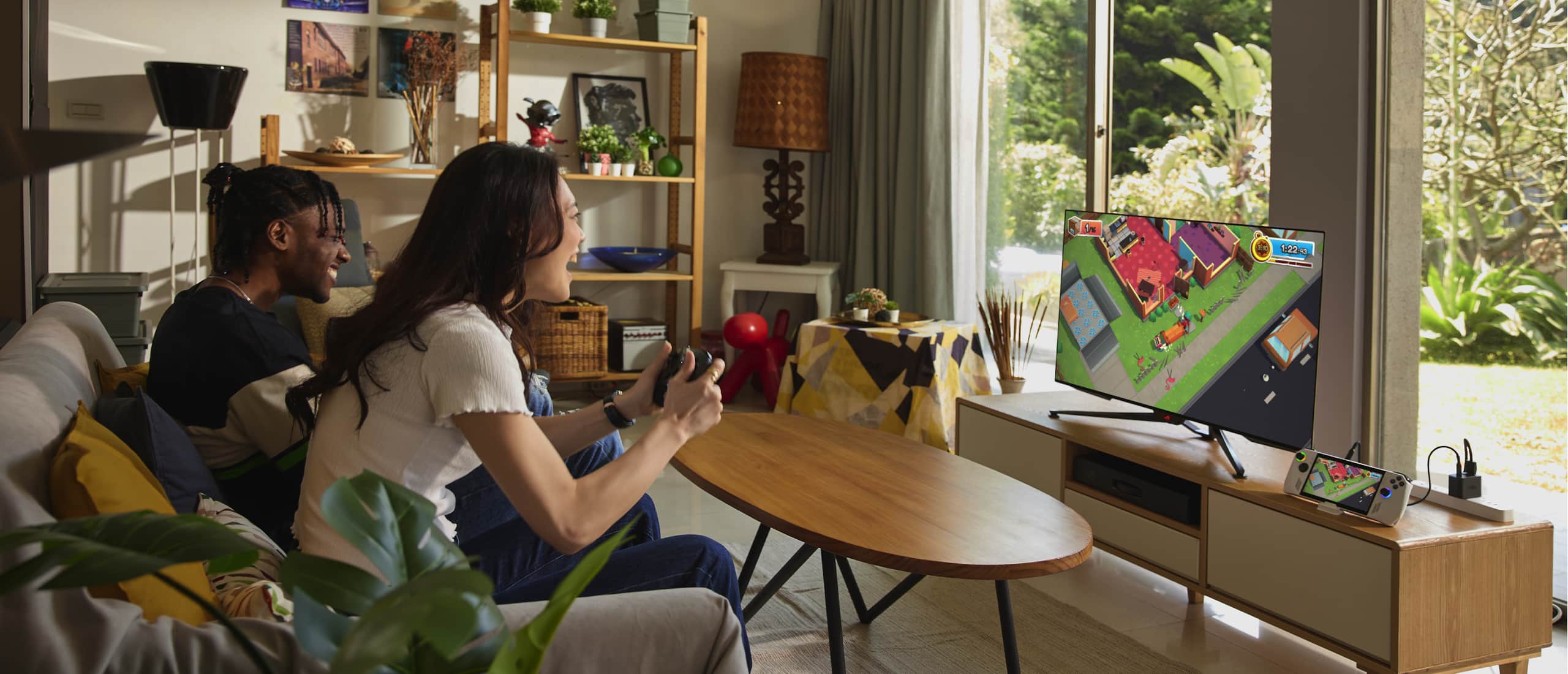 Два человека сидят на диване в гостиной. Подключив консоль ROG Ally к телевизору, они играют вместе в мультиплеере. 
