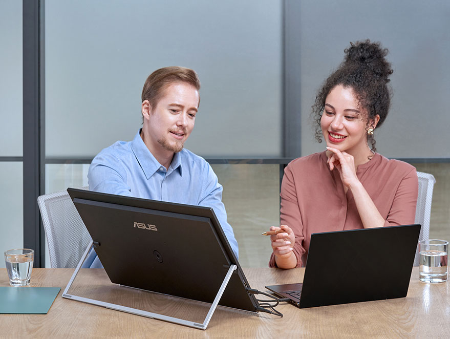 Een moderne professional werkt in de woonkamer aan een lage cafétafel, met een laptop en een ZenScreen MB249C draagbare monitoropstelling, in kickstand-modus