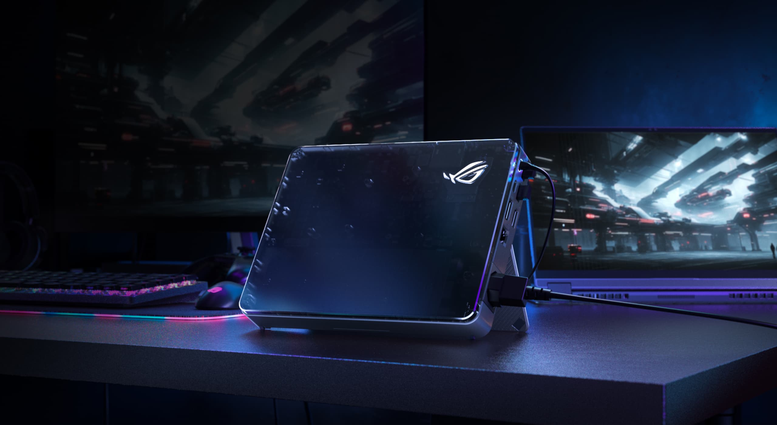 A view of 2025 XG Mobile in the center of a desk with an ROG logo on its front cover. There are also a screen and Flow X13 in the background.