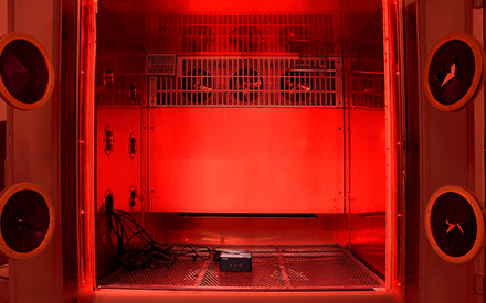 A small black computer box placed inside an environment that resembles an oven, illuminated with a red hue.