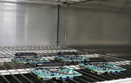 Four green and black electronic components placing in a oven-like environment on a wire mesh