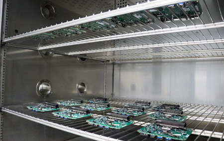 eleven green and black electronic components are placed in an oven-like environment on a wire mesh.