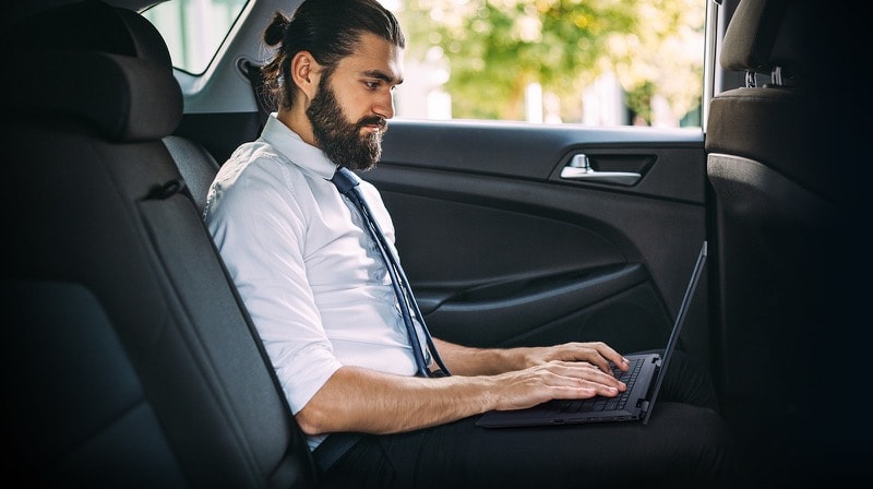 Side-view of a bearded mand using an ExpertBook B7 Flip in the backseat of a moving car. 