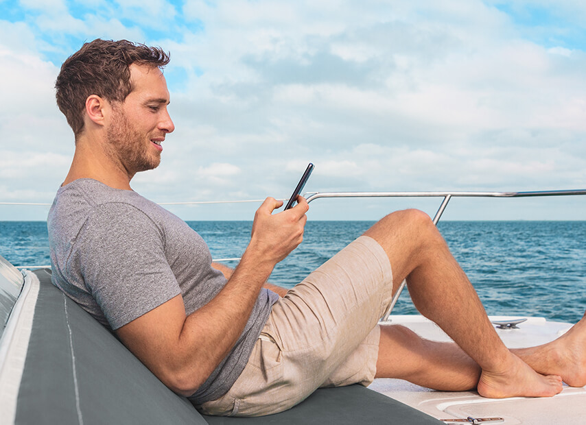 Egy férfi egy hajó fedélzetén lazít az okostelefonját használva.
