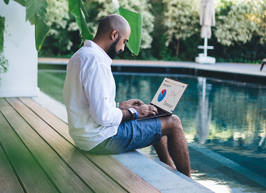 Egy férfi dolgozik a laptopján egy hotel úszómedencéje mellett ülve.