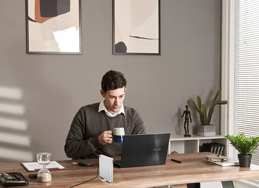 Egy férfi otthon használja a laptopját, az RT-AX57 Go router pedig az íróasztalon áll.