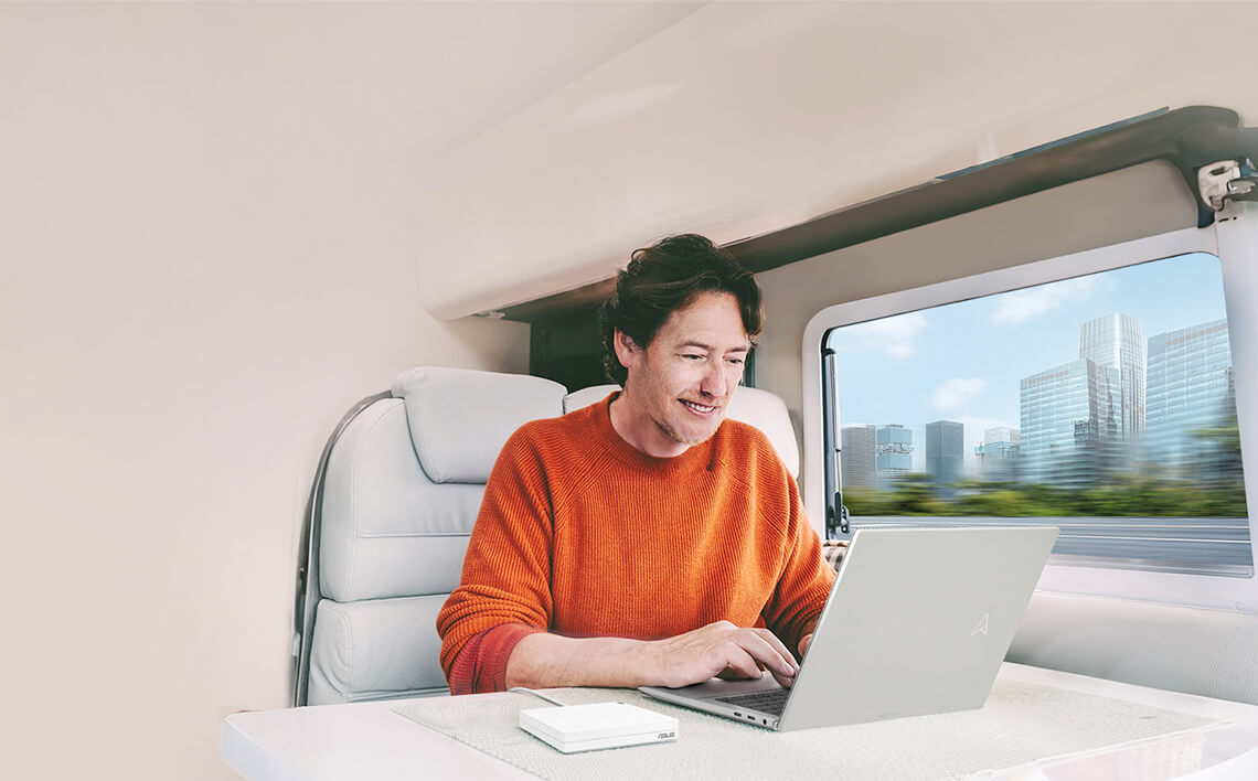 Un hombre utiliza un ordenador portátil en un tren en movimiento, con un RT-AX57 Go sobre la mesa y el paisaje cambiante visible a través de la ventana.