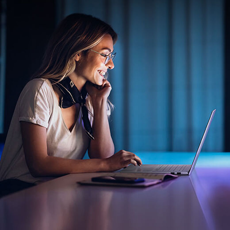 A smiling woman uses an ASUS Vivobook S 15 laptop in a dark room