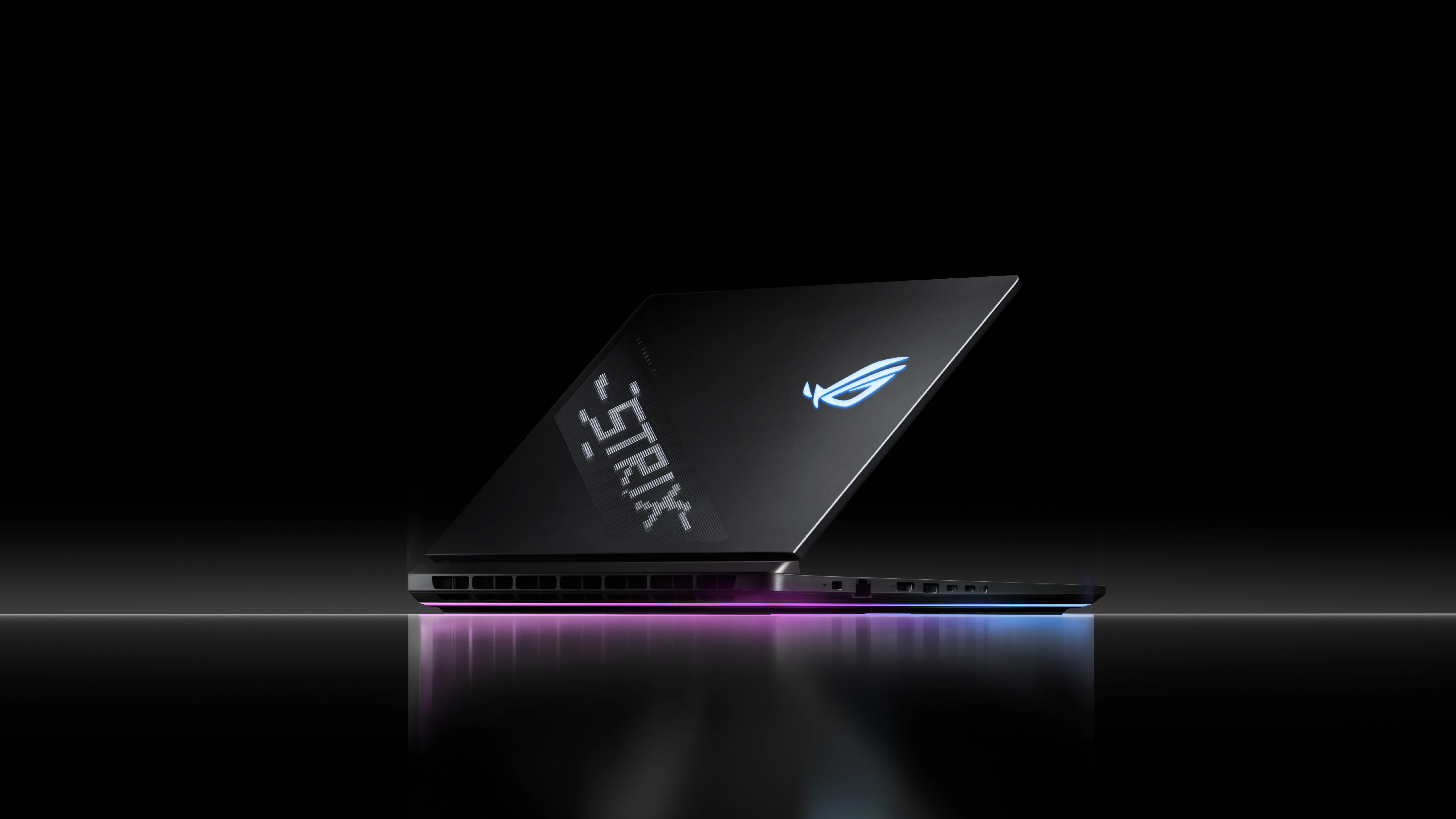 A Strix laptop sitting on a reflective surface with AniMe Vision and Full-surround RGB visible