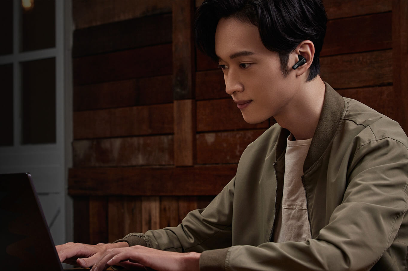 A man working on a laptop on a café patio, wearing ROG Cetra True Wireless