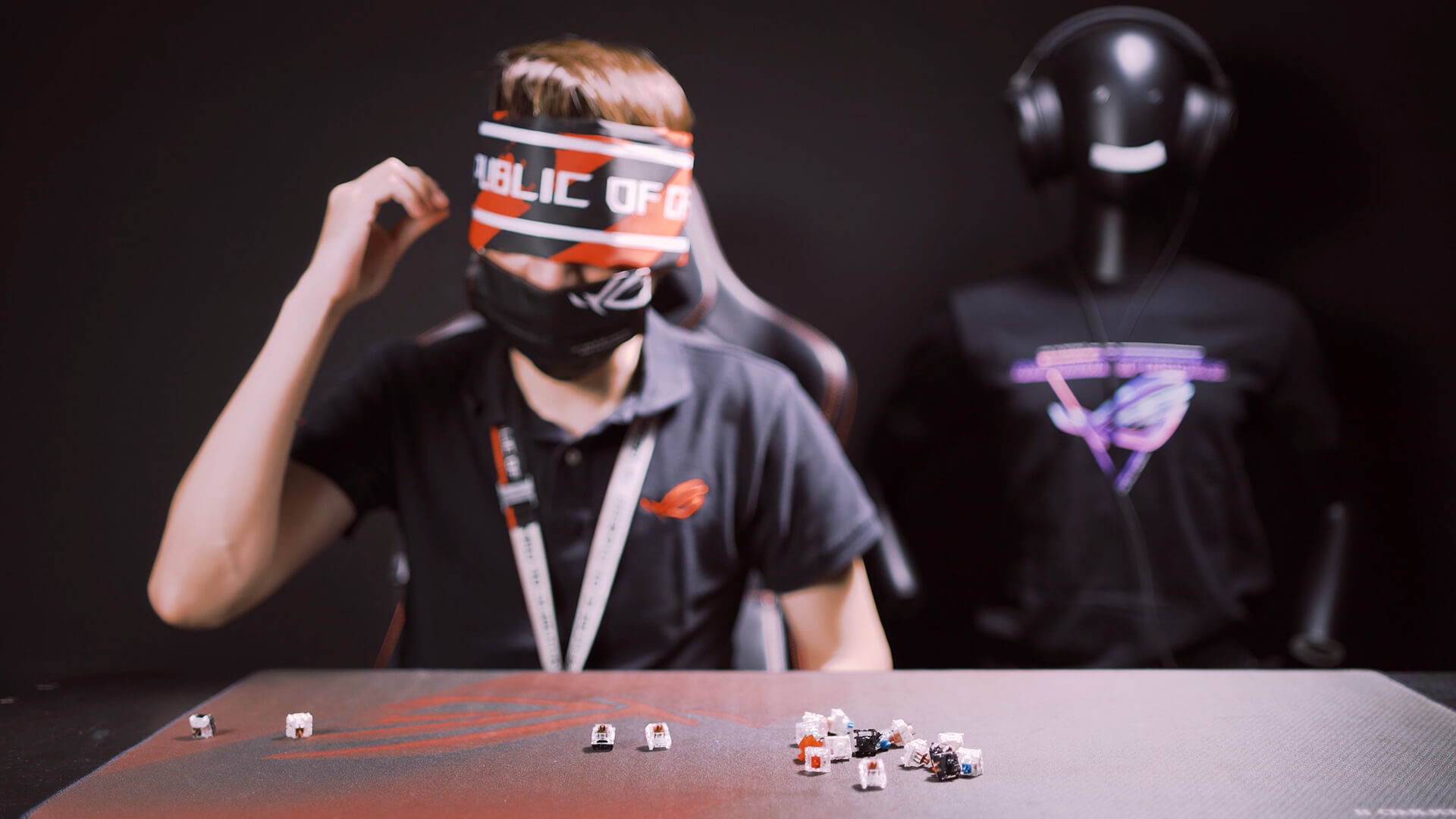 A guy with eye covered, holding a keyboard switch by his ear