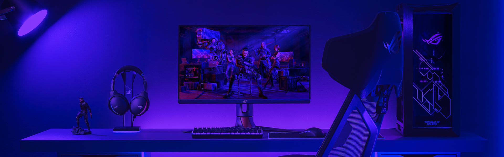ROG gaming monitor setup with a PC, one keyboard and mouse, and a headset on the desk