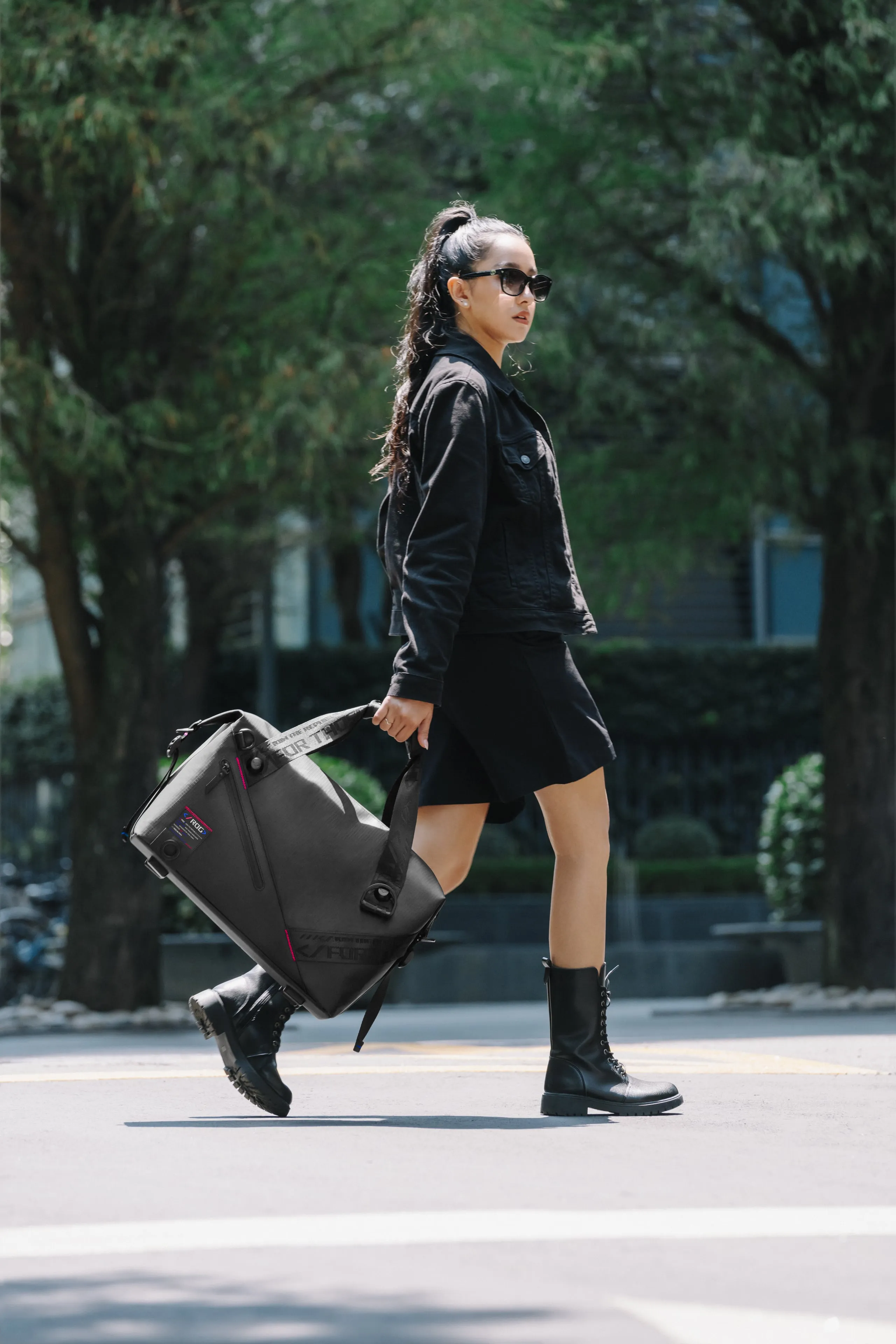 Woman in all black and sunglasses, walking on a street with the ROG SLASH Duffle Bag in her hand