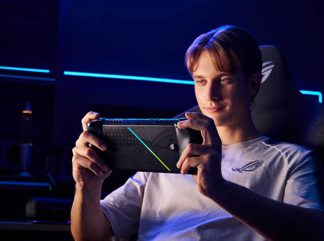 A person reclining in a computer chair in a dark room, playing with the ROG Ally X.