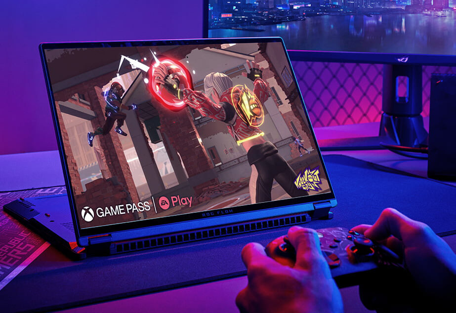 Den bärbara datorn ROG Flow X16 placerad på ett skrivbord i stativläge, med ett spel på skärmen och två händer som håller i en Xbox-handkontroll.