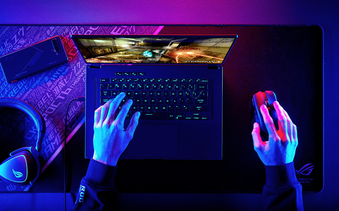 ROG Flow X16-laptop på et skrivebord, med én hånd hver på tastaturet og musen og et spill på skjermen.