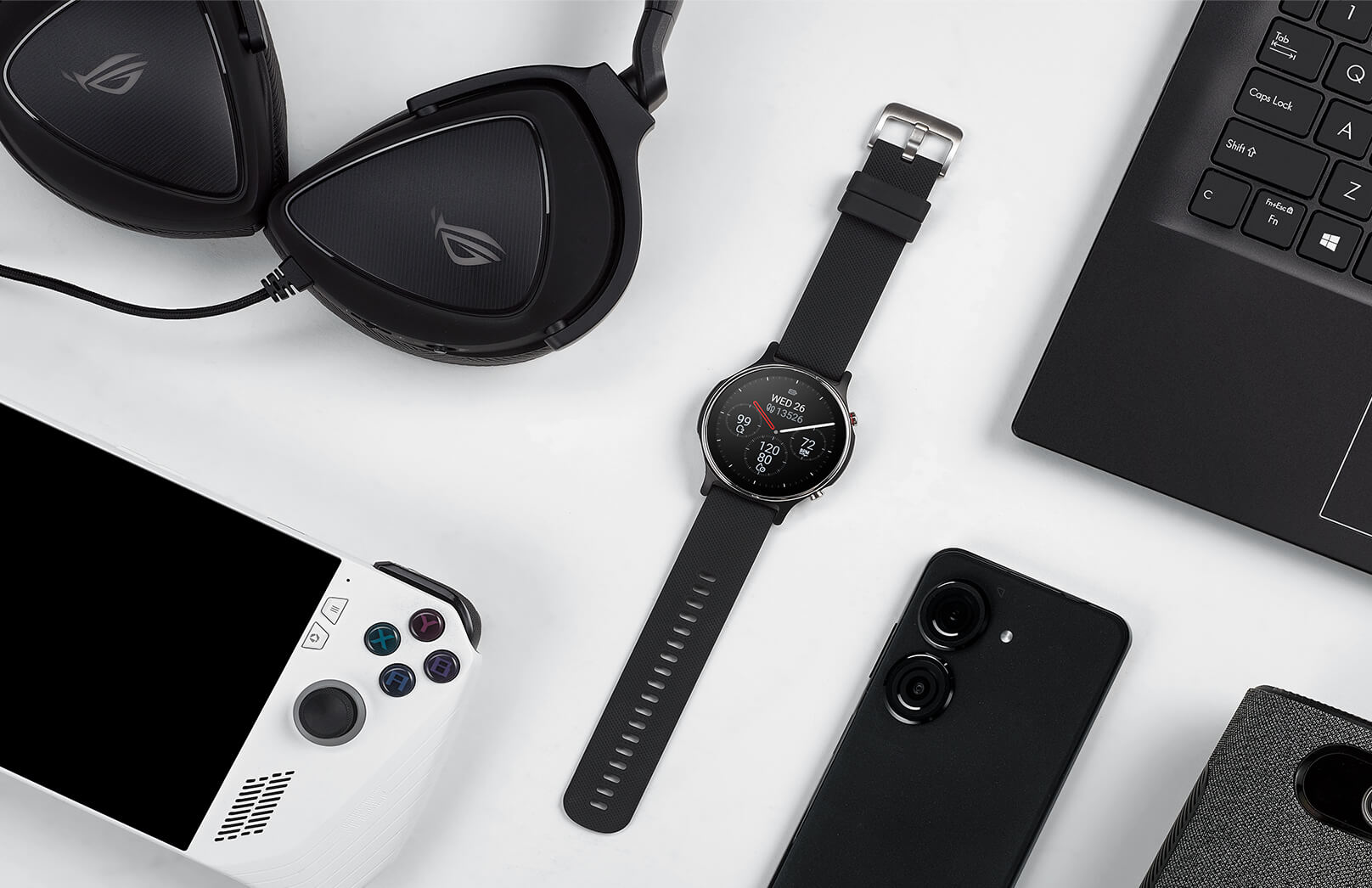On the white table there are gaming headset, game console, ASUS VivoWatch 6, smart phone and notebook from left to right side