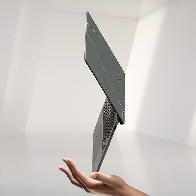 Een Zenbook S 13 OLED laptop in de kleur Basalt Gray balanceert op een van zijn hoeken op de hand van een persoon, met witte muren op de achtergrond