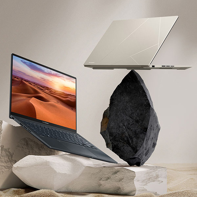 Two Zenbook 14X OLED laptops in Inkwell Gray and Sandstone Beige colors balancing on rocks with sand in the background