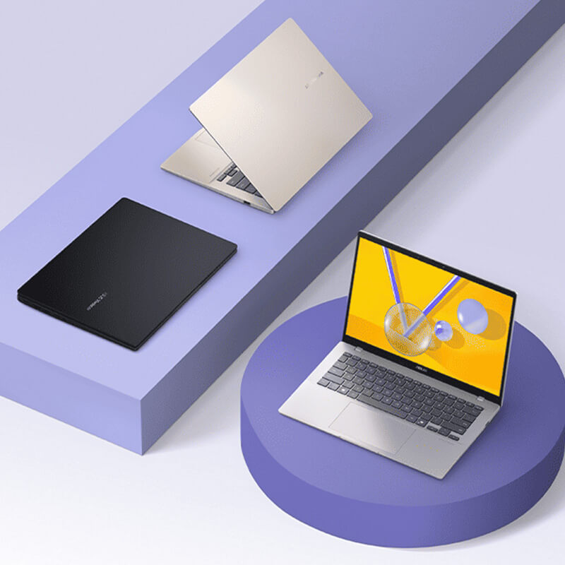 Three ASUS Vivobooks sit on purple geometric shapes. The platinum gold model is slightly open, the black model is closed, and the silver model is open.