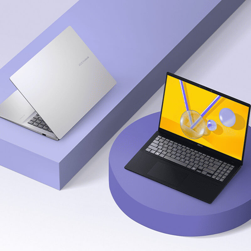 Two ASUS Vivobooks sit on purple geometric shapes. The silver model is slightly open and oriented to the left while the black model is open and facing forward.