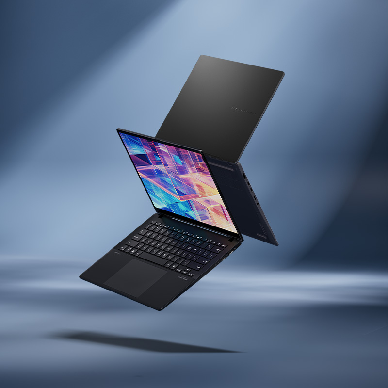 Two open laptops sit on a geometric stand. The black laptop is hovering above two books while a blue vase with a yellow flower sits on the right.