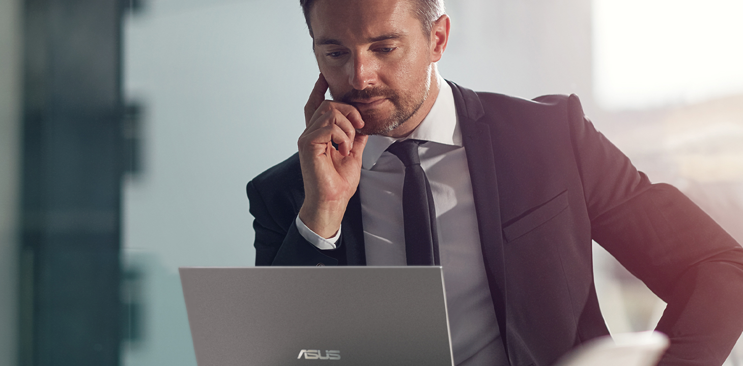 A businessman is attentively looking at the ASUS laptop on a desk.