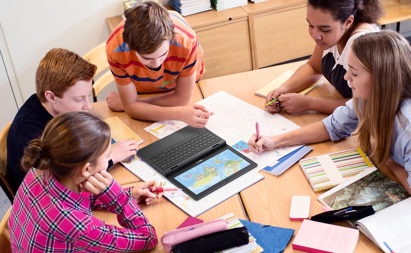 Een bovenaanzicht van 5 leerlingen die aan een tafel in het klaslokaal zitten en kijken naar een afbeelding op de ASUS Chromebook CR11 die volledig 180 graden is geopend en plat op het bureau is gelegd.