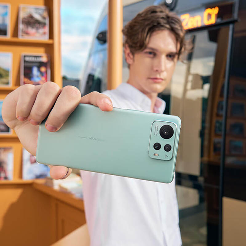 a man holding an ASUS Zenfone 12 Ultra (Sage Green), standing in front of a bookshelf.