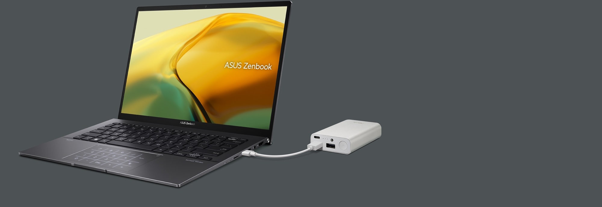 Zenbook 14 OLED in Jade Black, opened at 45 degrees and viewed from the rear. It is being charged via USB from a black power bank.