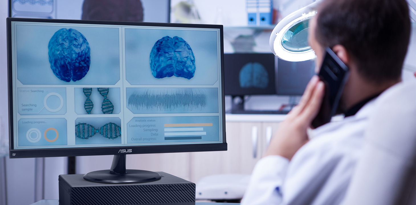 Terveydenhuollon työntekijä katselee aivojen kuvannusta ja analyysitietoja ASUS ExpertCenter-pöytäkoneen näytöltä ja puhuu samalla kännykkään.