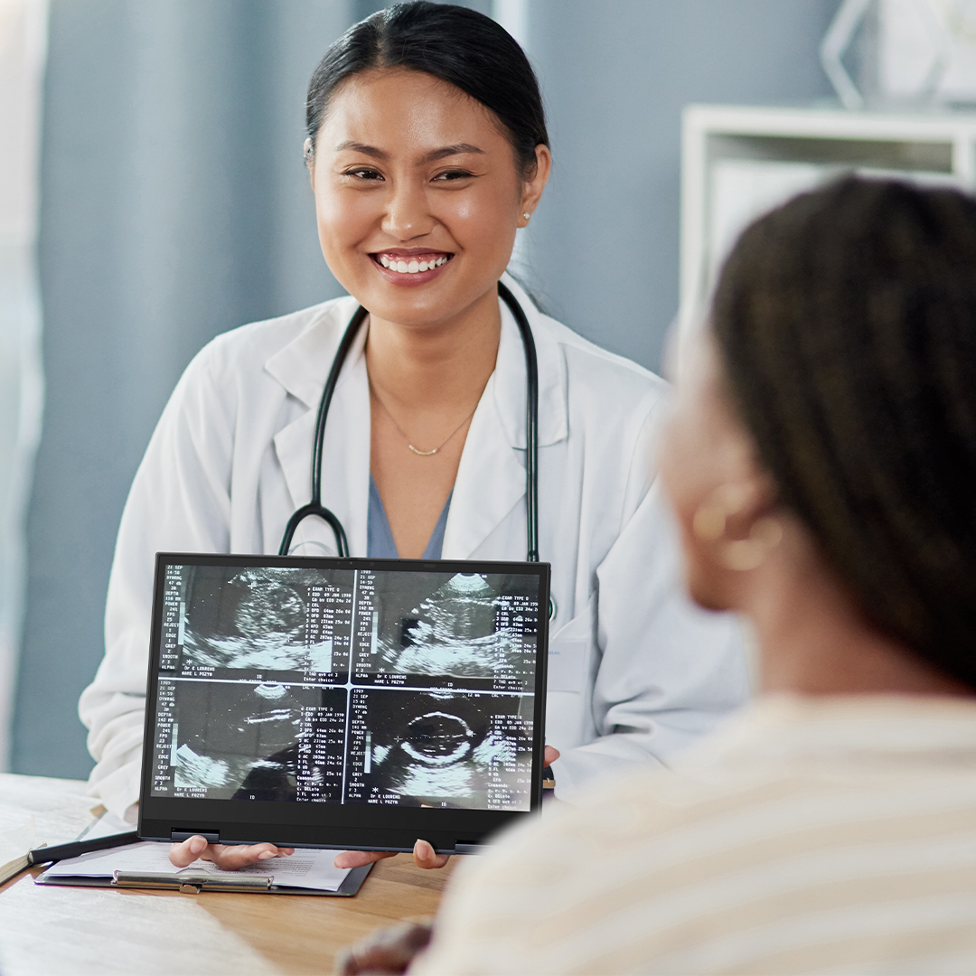 Un médico muestra fotos de ultrasonido de la computadora portátil ASUS ExpertBook a una pareja. Todos ellos están sonriendo.